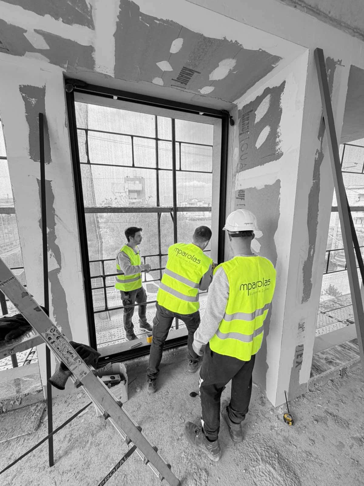 Mparolas installation team positioning a large aluminium window frame at the MOB1 project before final alignment.